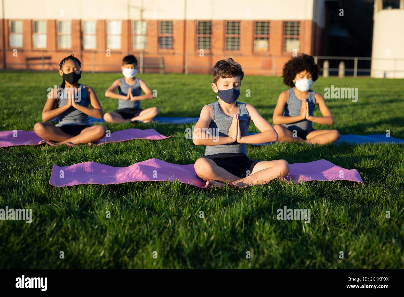 Group of kids wearing face masks performing yoga in the garden Stock Photo