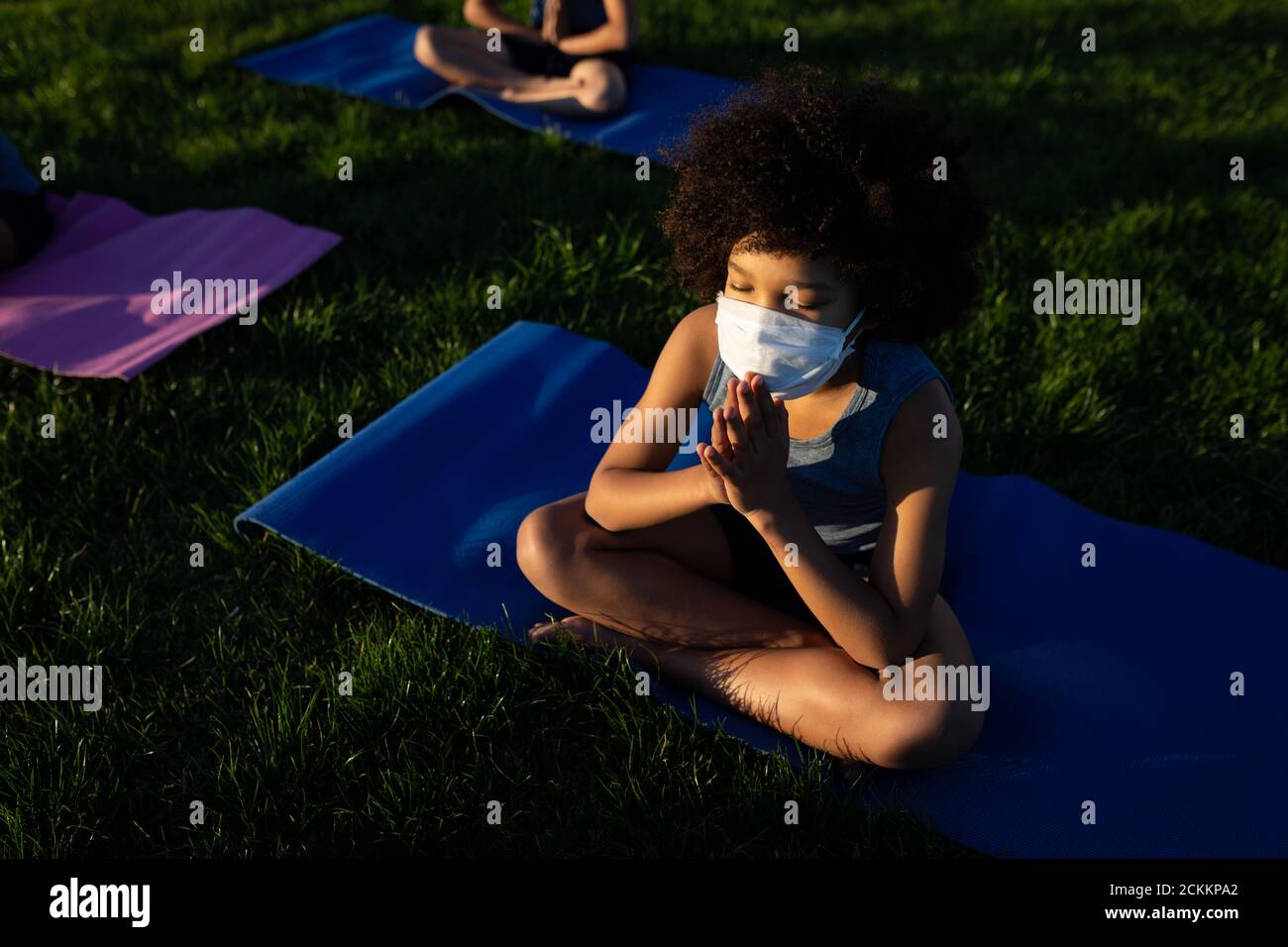 Overhead view of boy wearing face mask performing yoga in the garden Stock Photo