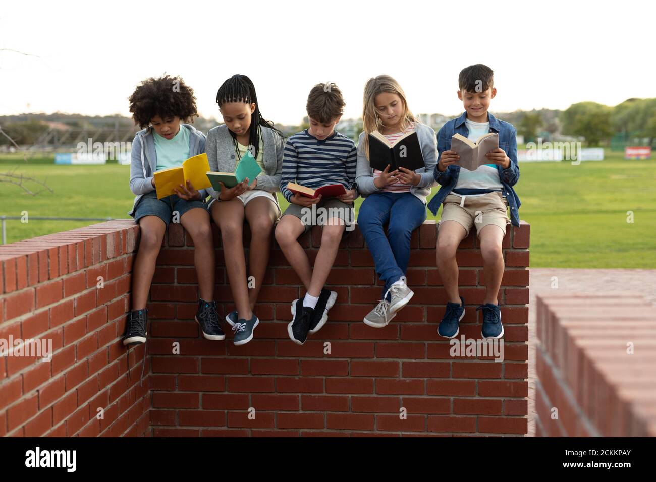Group of kids reading books while sitting on a brick wall Stock Photo