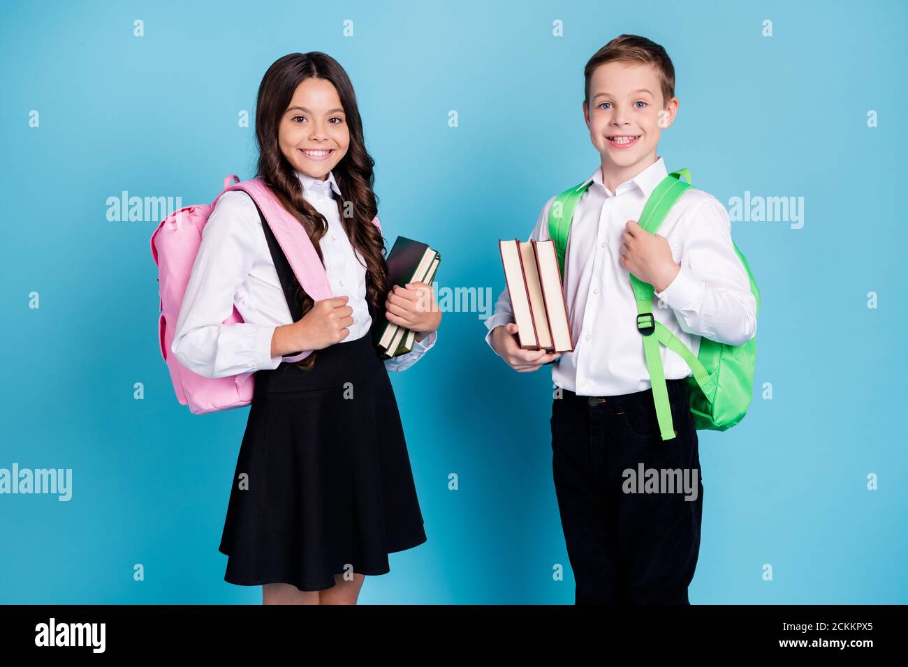 Photo of two small girl boy schoolchildren brother sister classmates hold books walk library study year finishing wear backpack white shirt black Stock Photo