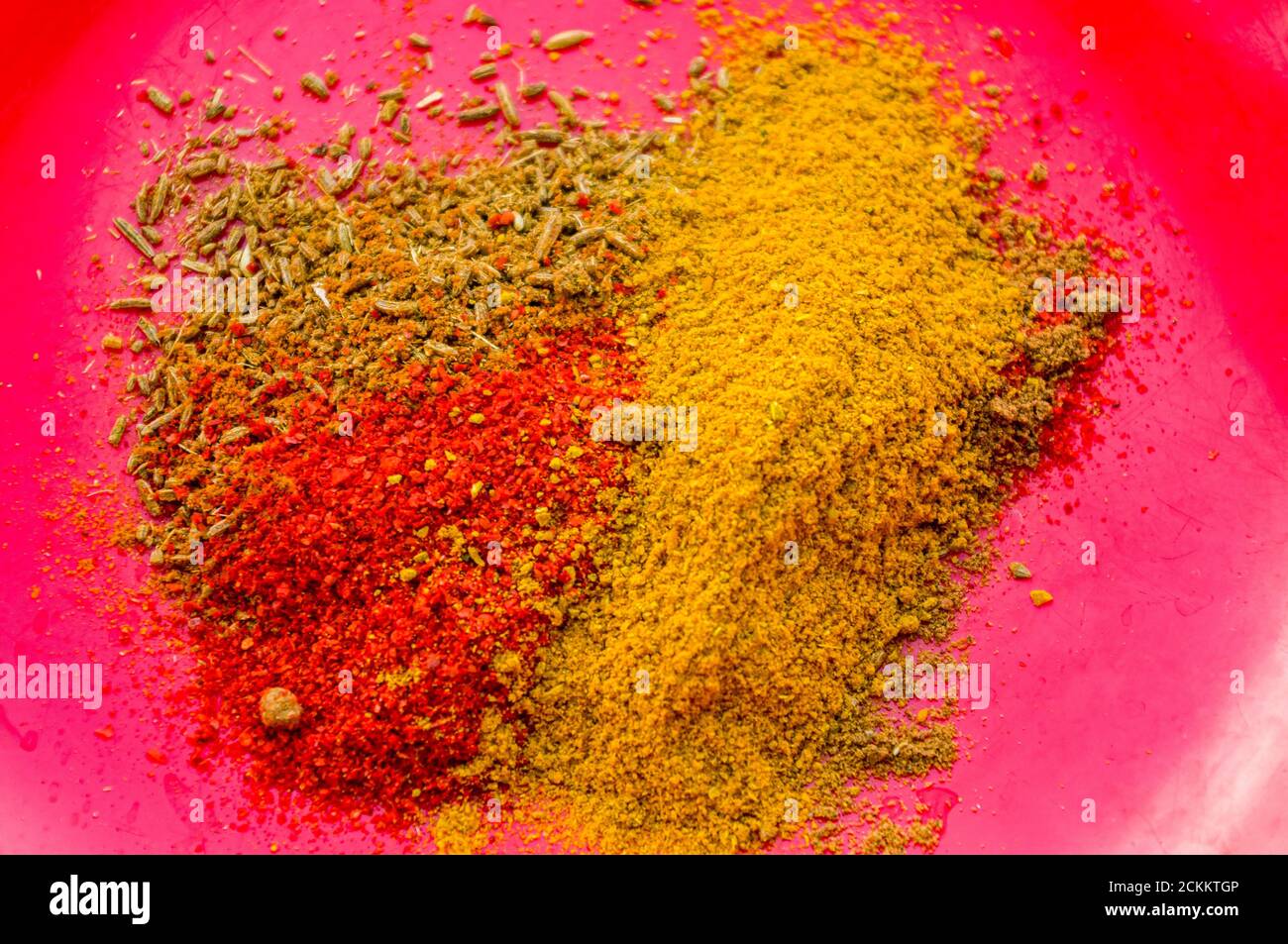 Spices red pepper, ground coriander, salt and turmeric on a red plate