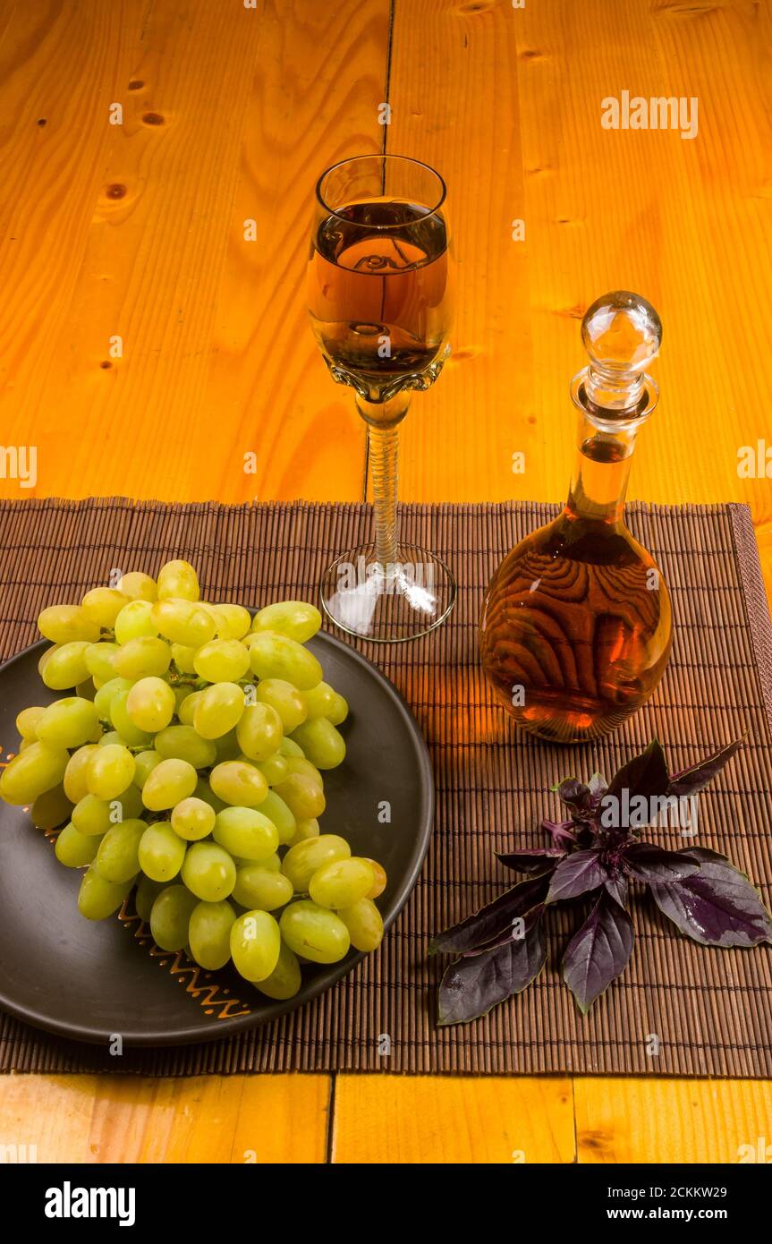 large brush of green grapes in a ceramic plate, a decanter and a glass of wine and cheese Stock Photo