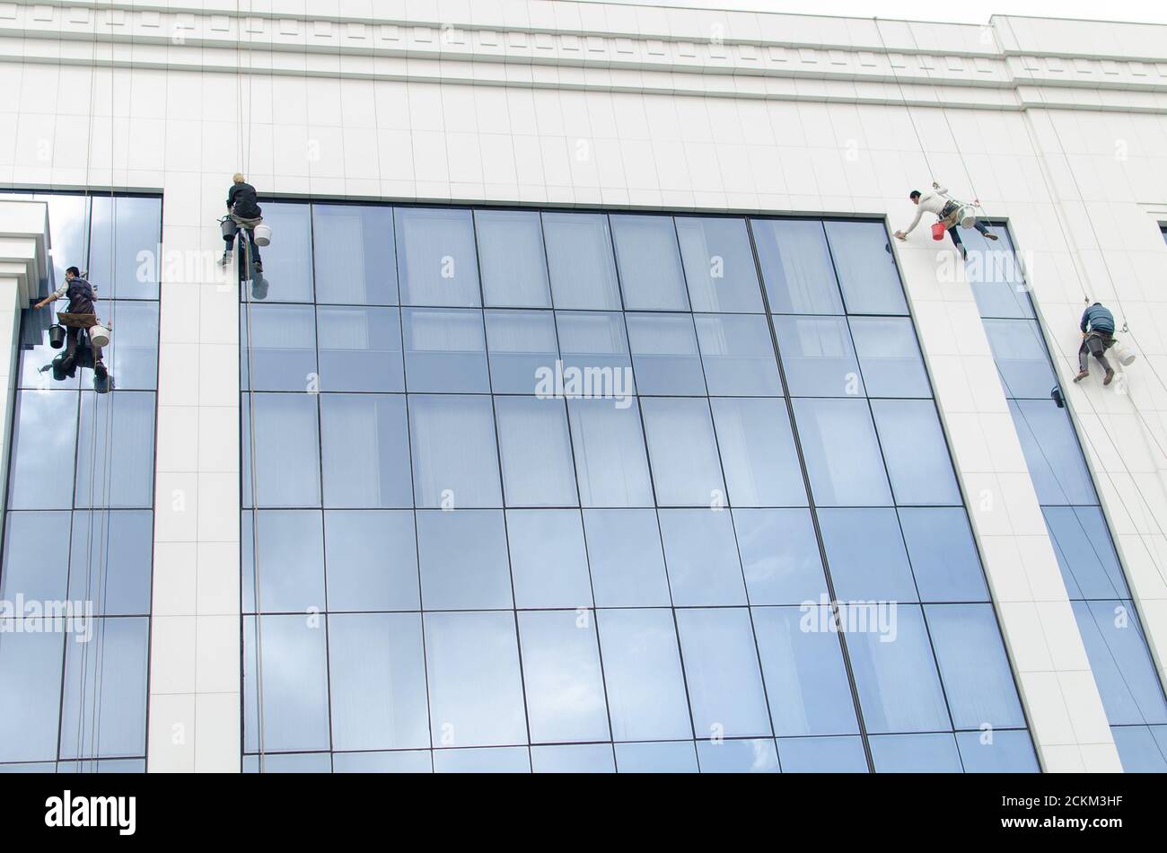 Four people climber, descended on cables from the roof of the building with buckets and rags, and wash the building Stock Photo