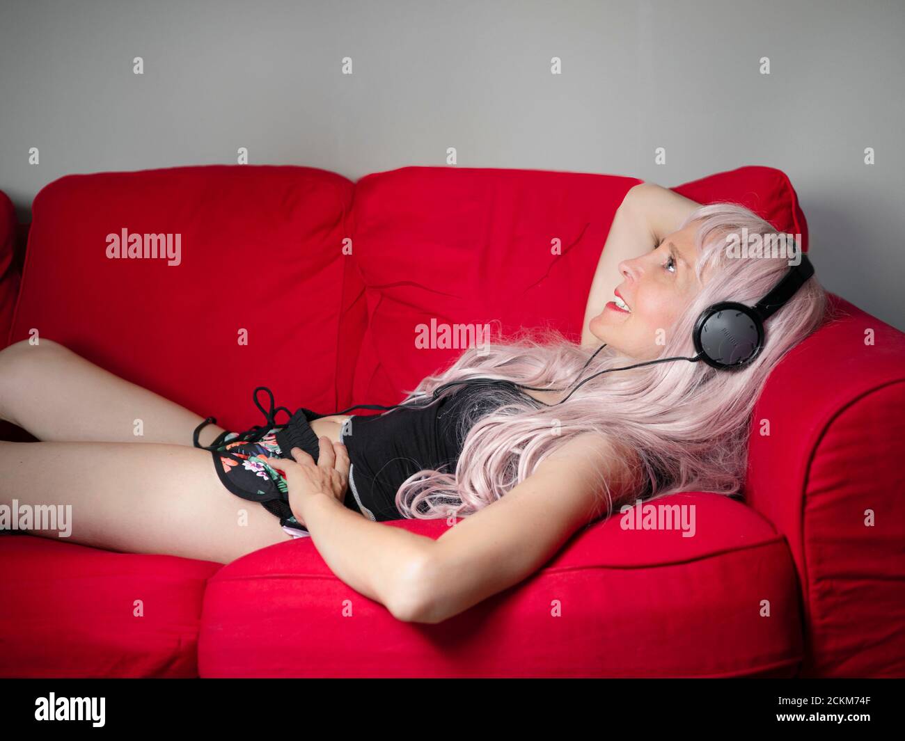 horizontal profile portrait of a smiling caucasian woman with headphone lying on a red sofa Stock Photo