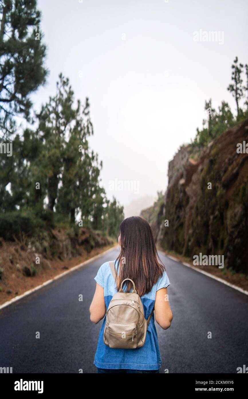 Rear view of long hair brunette girl walking on the foggy road in the ...
