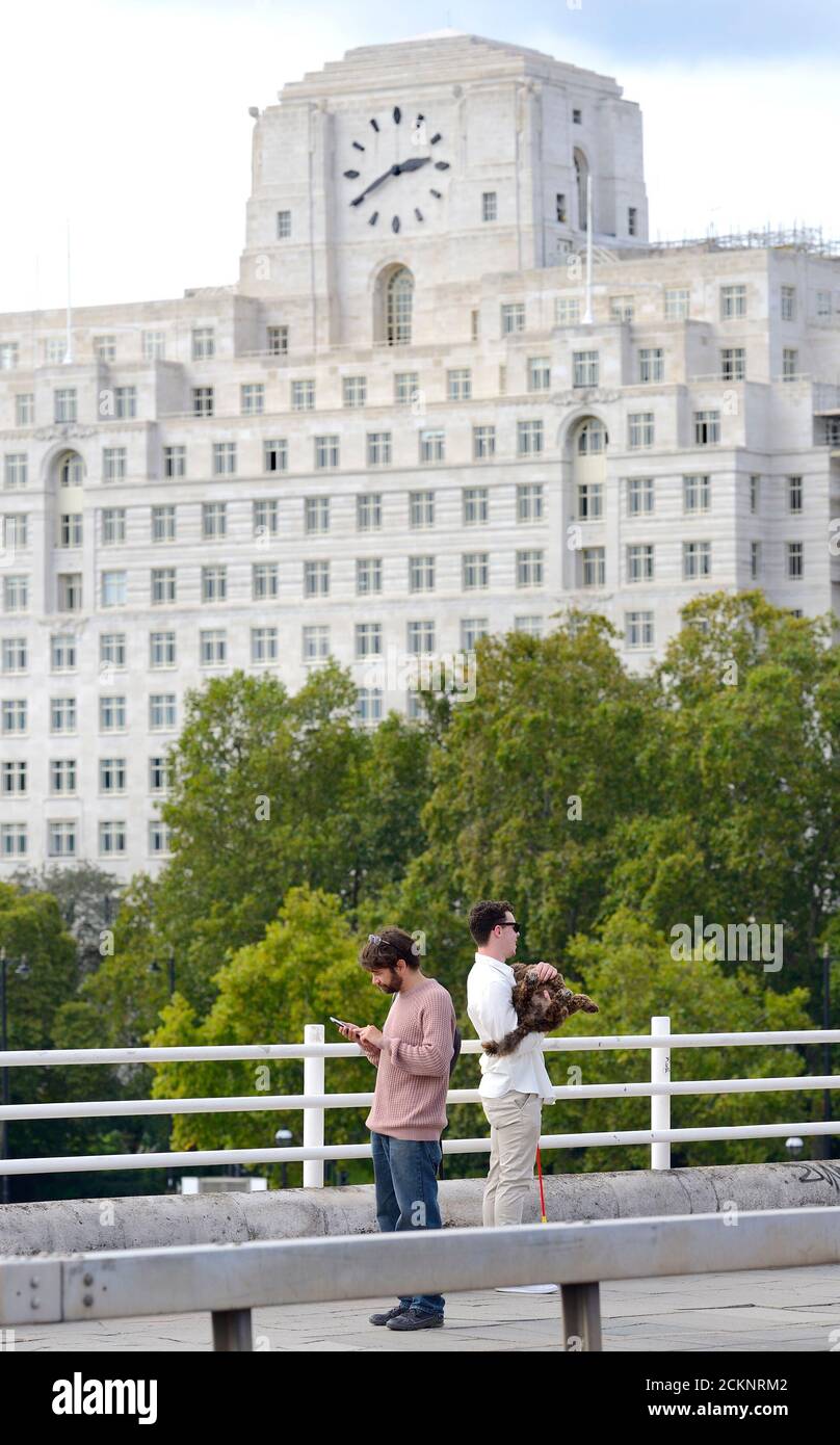 London, England, UK. A man on his phone and another holding his dog (for a photo) on Waterloo Bridge. Shell Mex House (80 Strand) behind Stock Photo