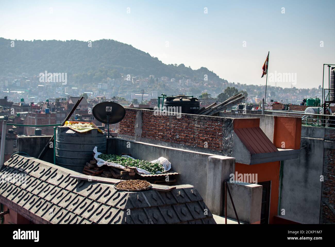 Bhaktapur, Kathmandu, Nepal - December 23, 2019: Cityscape view from a roof top over fruits and vegetables drying in the sun with the city in the back Stock Photo