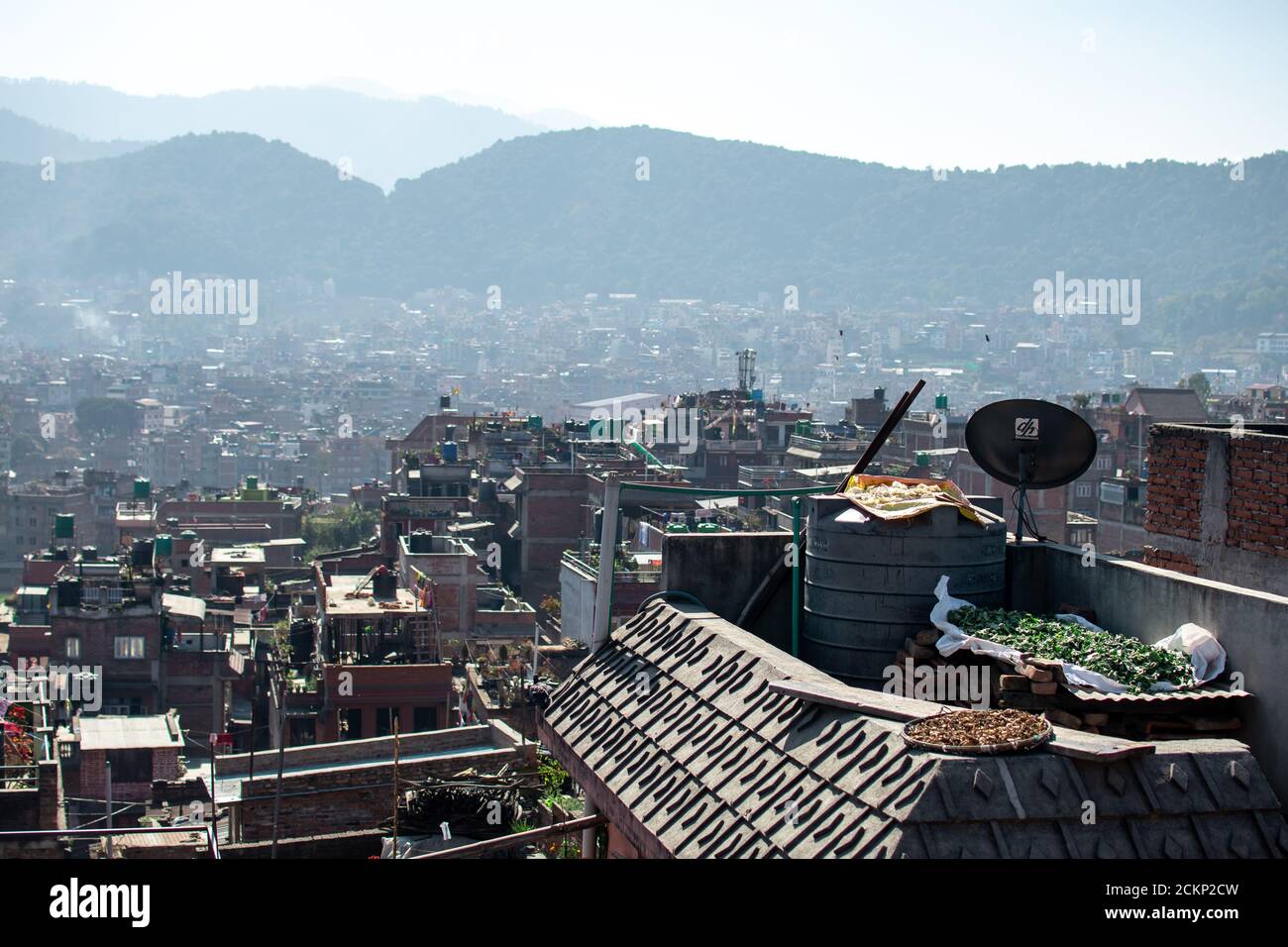 Bhaktapur, Kathmandu, Nepal - December 23, 2019: Cityscape view from a roof top over fruits and vegetables drying in the sun with the city in the back Stock Photo