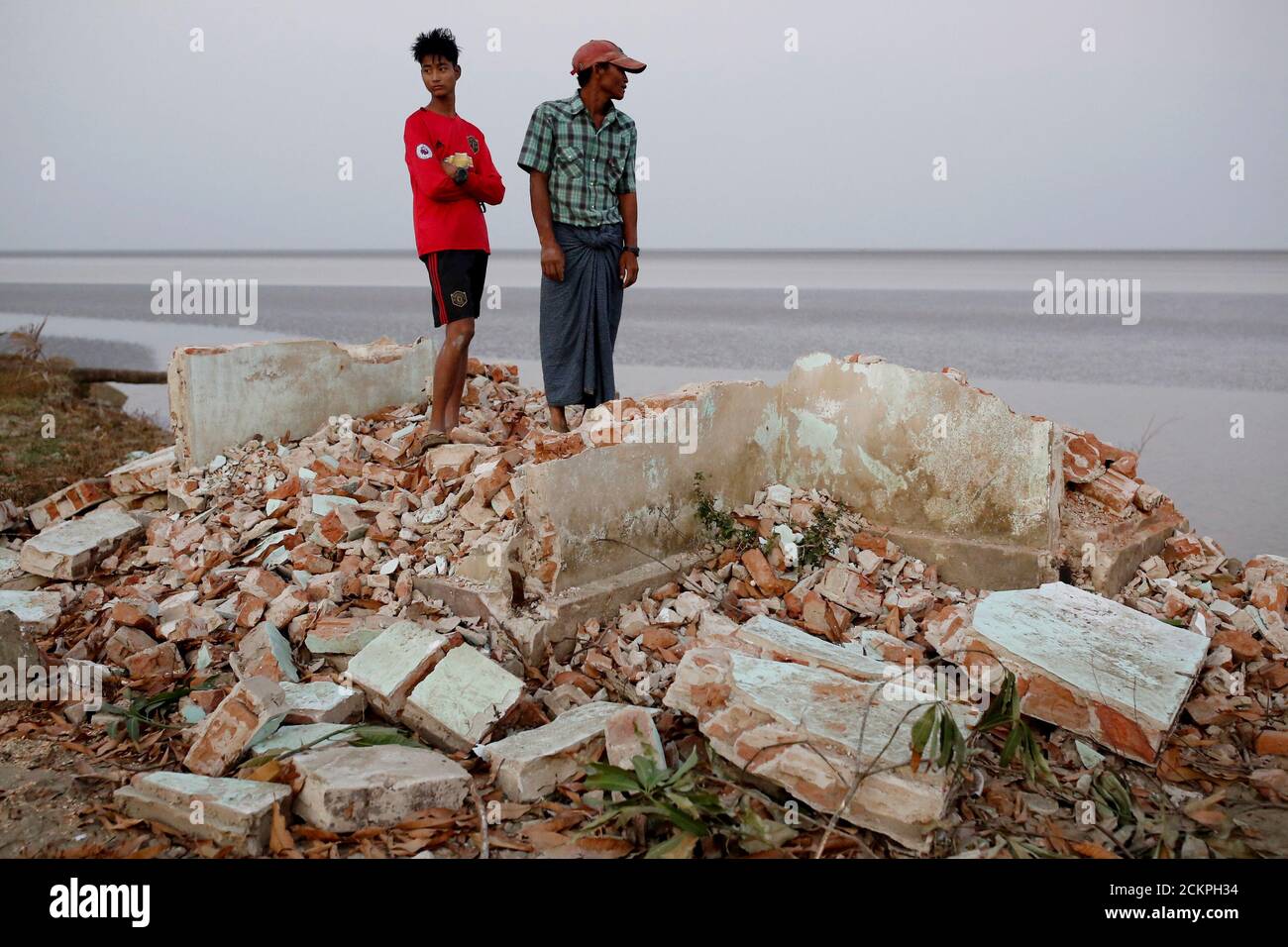 Myo Zaw, 15, and his father Aung So Oo, 45, stand at the ruins of a monastery after the riverbank it was located on collapsed into the water in Ta Dar U village, Bago, Myanmar, February 5, 2020. Photo taken on February 5, 2020. REUTERS/Ann Wang Stock Photo