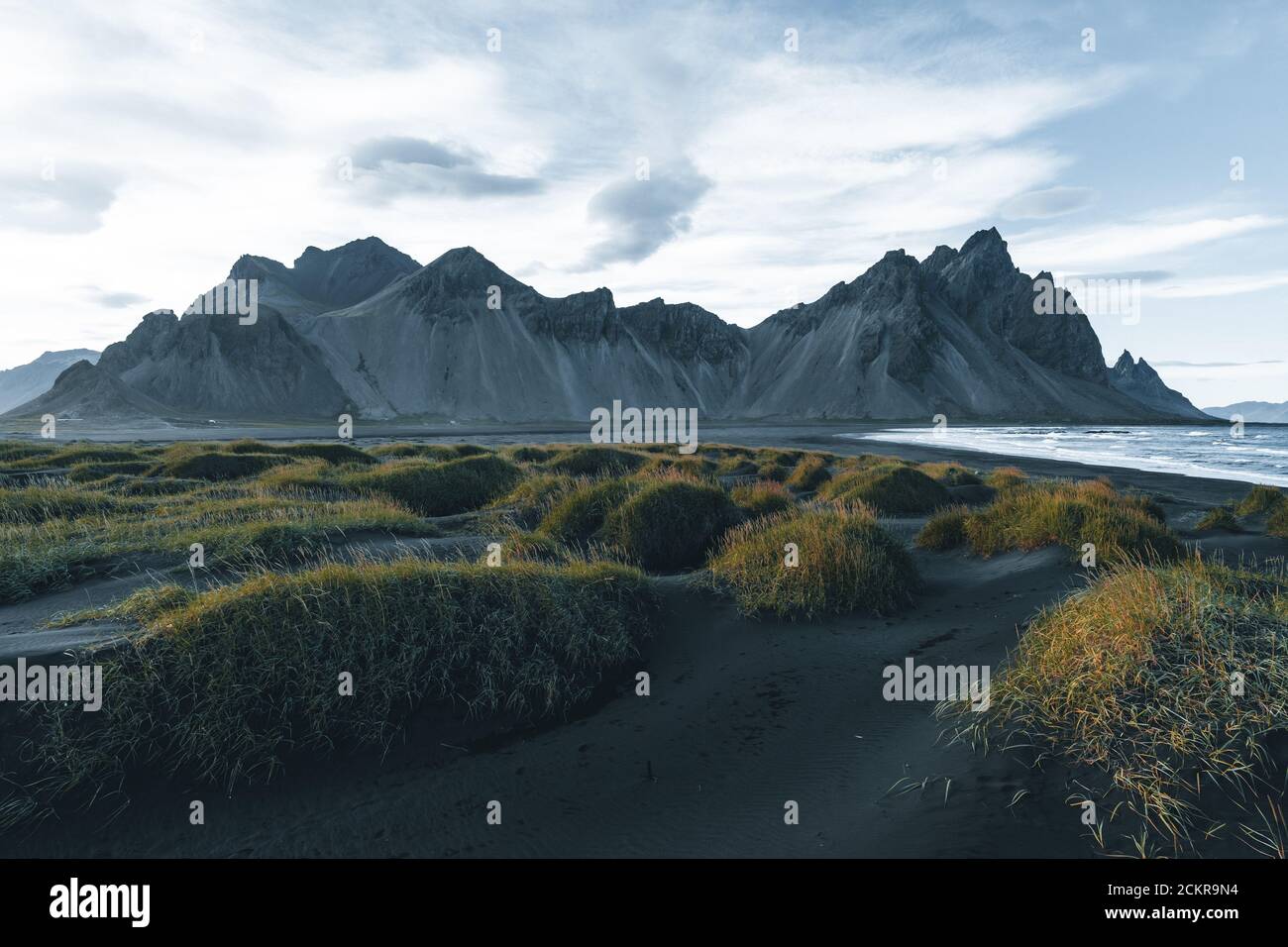 Sunny landscape of Iceland. Gorgeous view on Stokksnes cape and Vestrahorn Mountain with black sand with grass on foreground at summer. Iconic Stock Photo