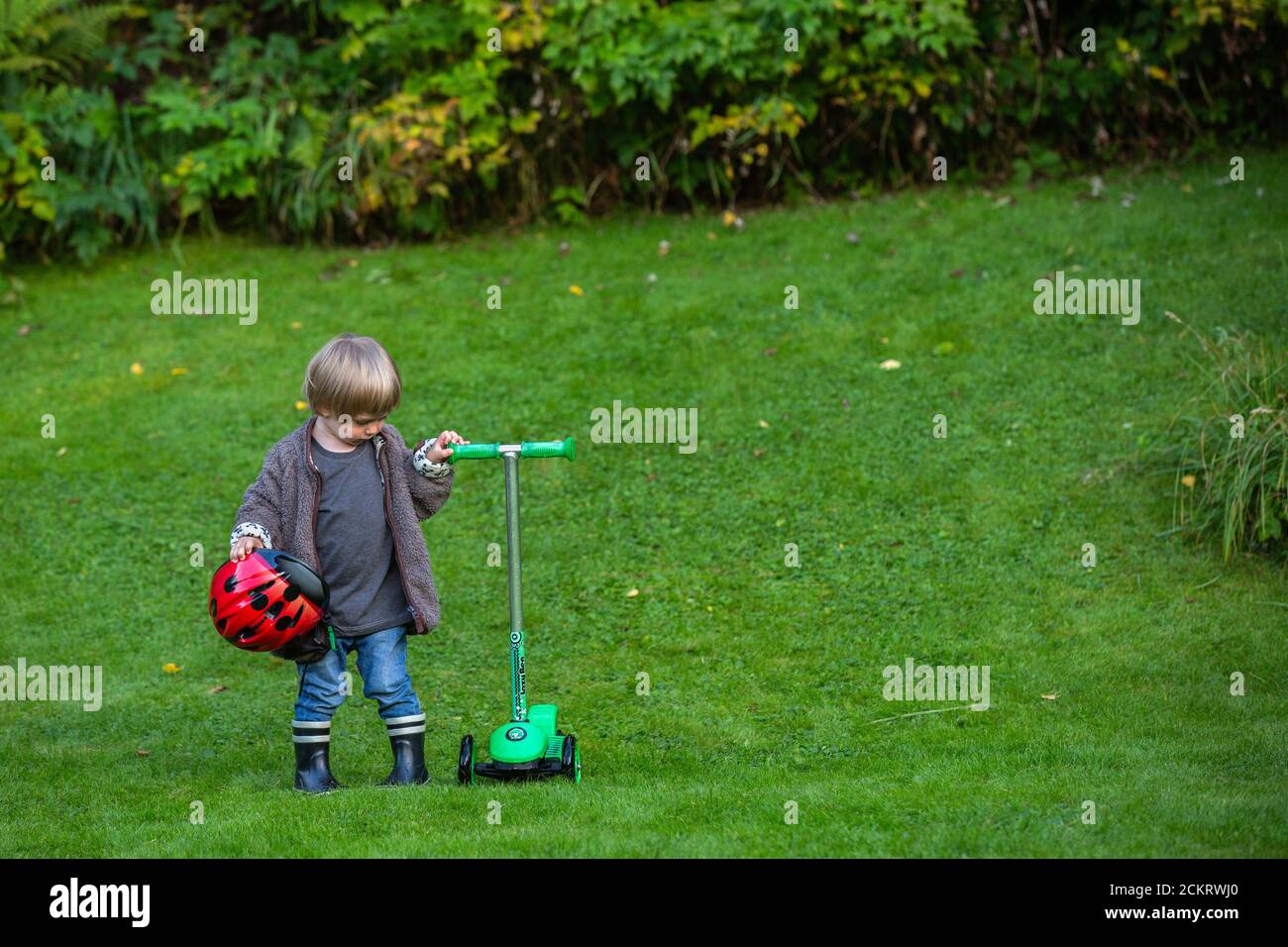 Young boy looking at his kick scooter in the garden and holding a bike helmet Stock Photo