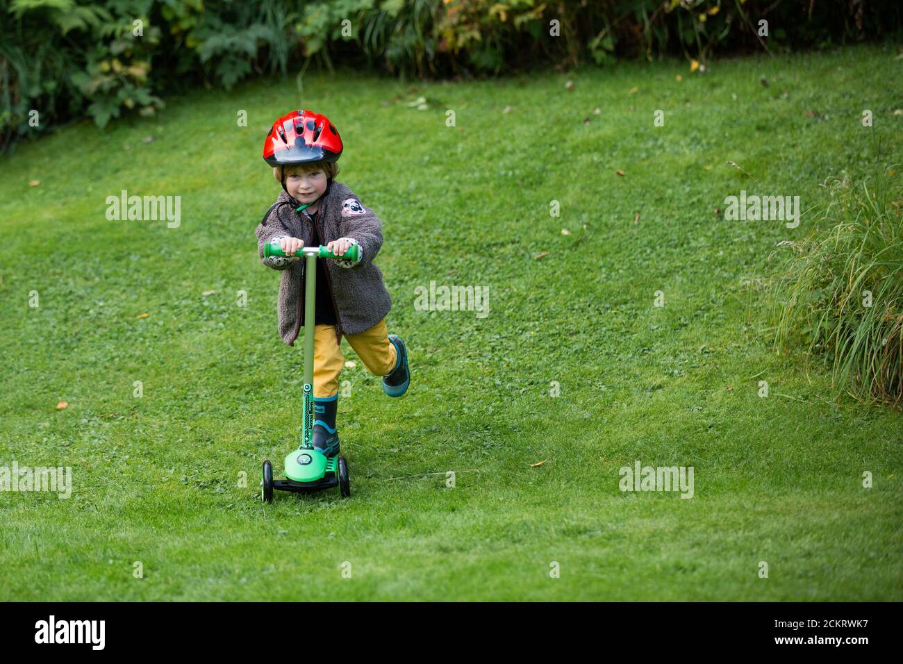 Young boy in the grass riding a kick scooter Stock Photo