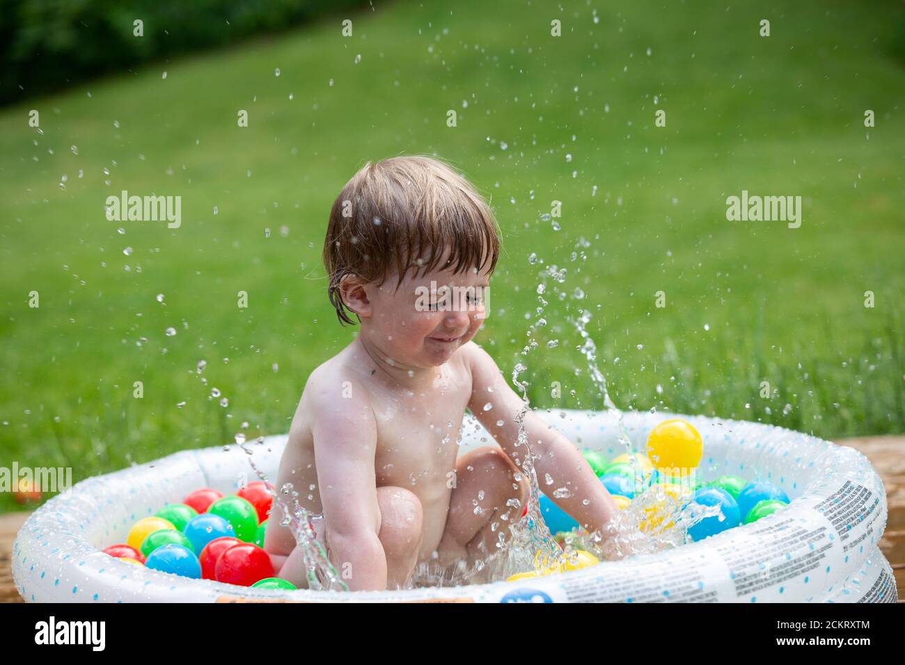 young boy splashing water in a tiny plastic pool outdoors in summer Stock Photo