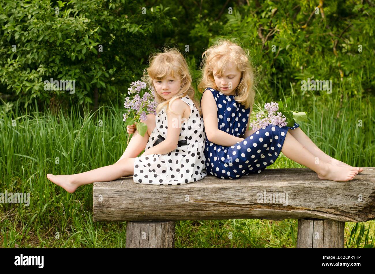 two beautiful blond girls sitting on bench in meadow Stock Photo