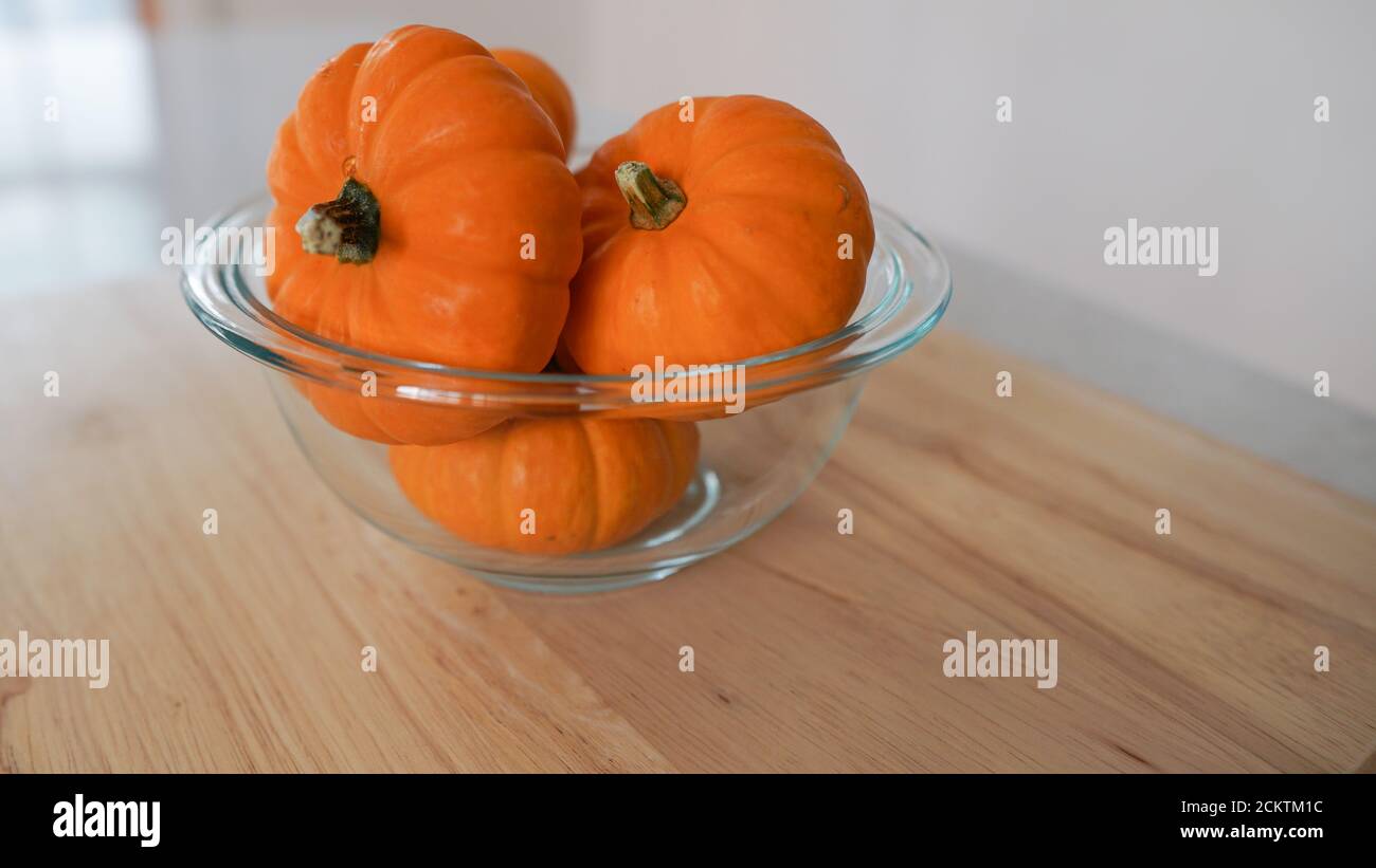 Glass bowl of miniature pumpkins on a wooden countertop. Background has space for copy. Stock Photo
