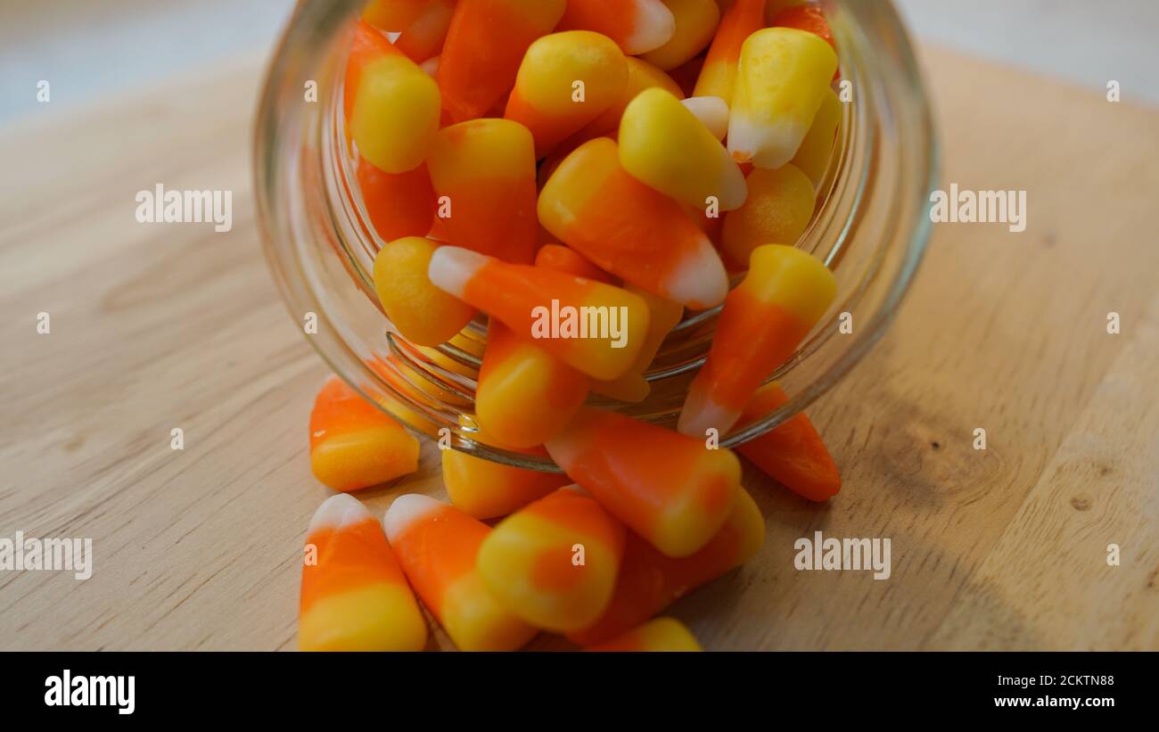 Up close view of candy corn spilling out of a glass jar onto a wooden countertop Stock Photo