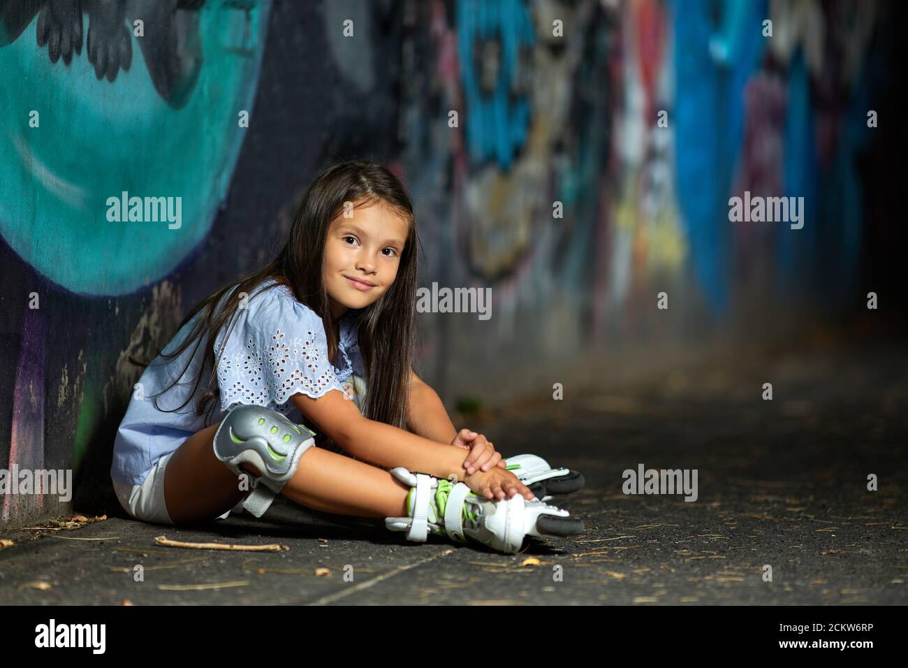 tired happy little child girl in roller skates is resting after rollerskating in park in the