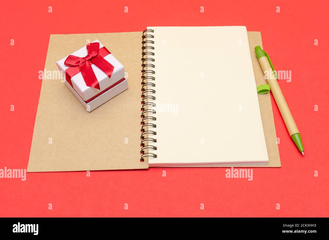 Notepad with pen and gift lies on a red background, copy space Stock