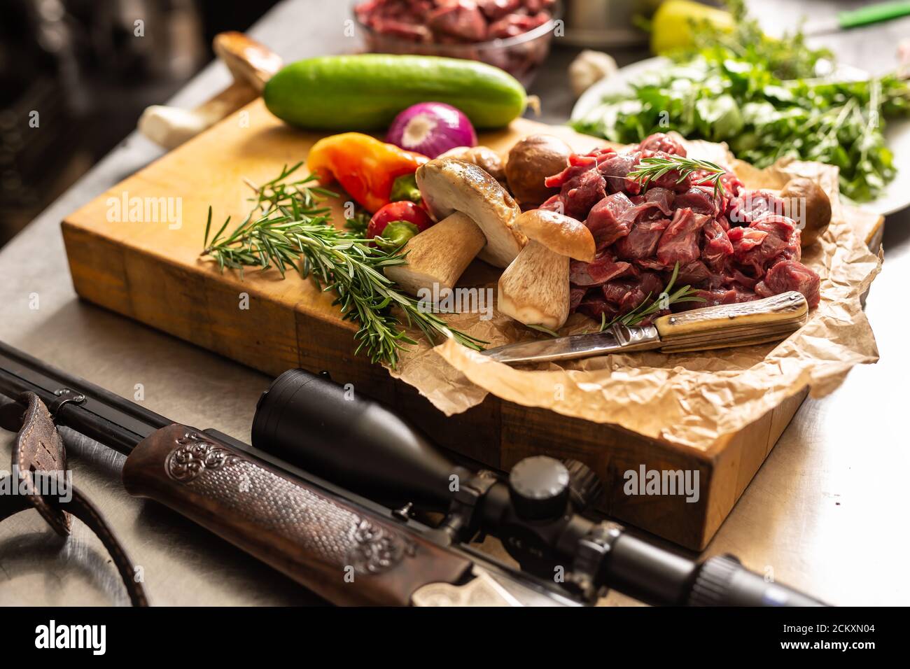 Sliced deer meat prepared for stew of game forest mushrooms herbs vegetables knife and hunter gun Stock Photo