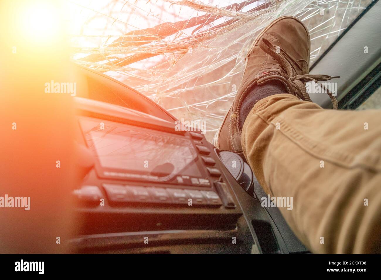 Foot on the dashboard on the background of the broken windshield of the