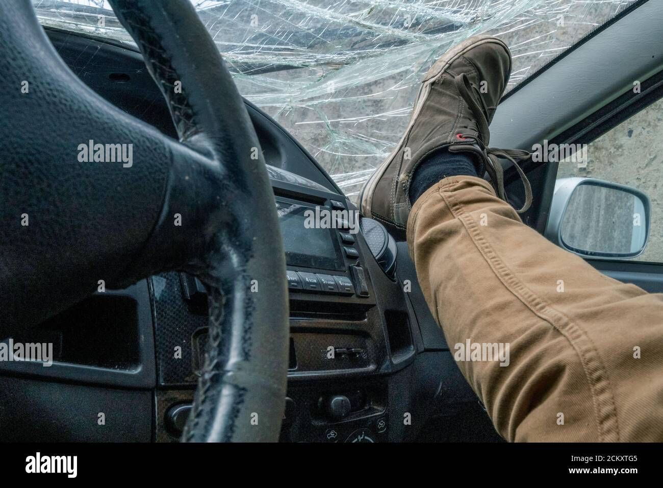 Foot on the dashboard on the background of the broken windshield of the car. Cracked windshield