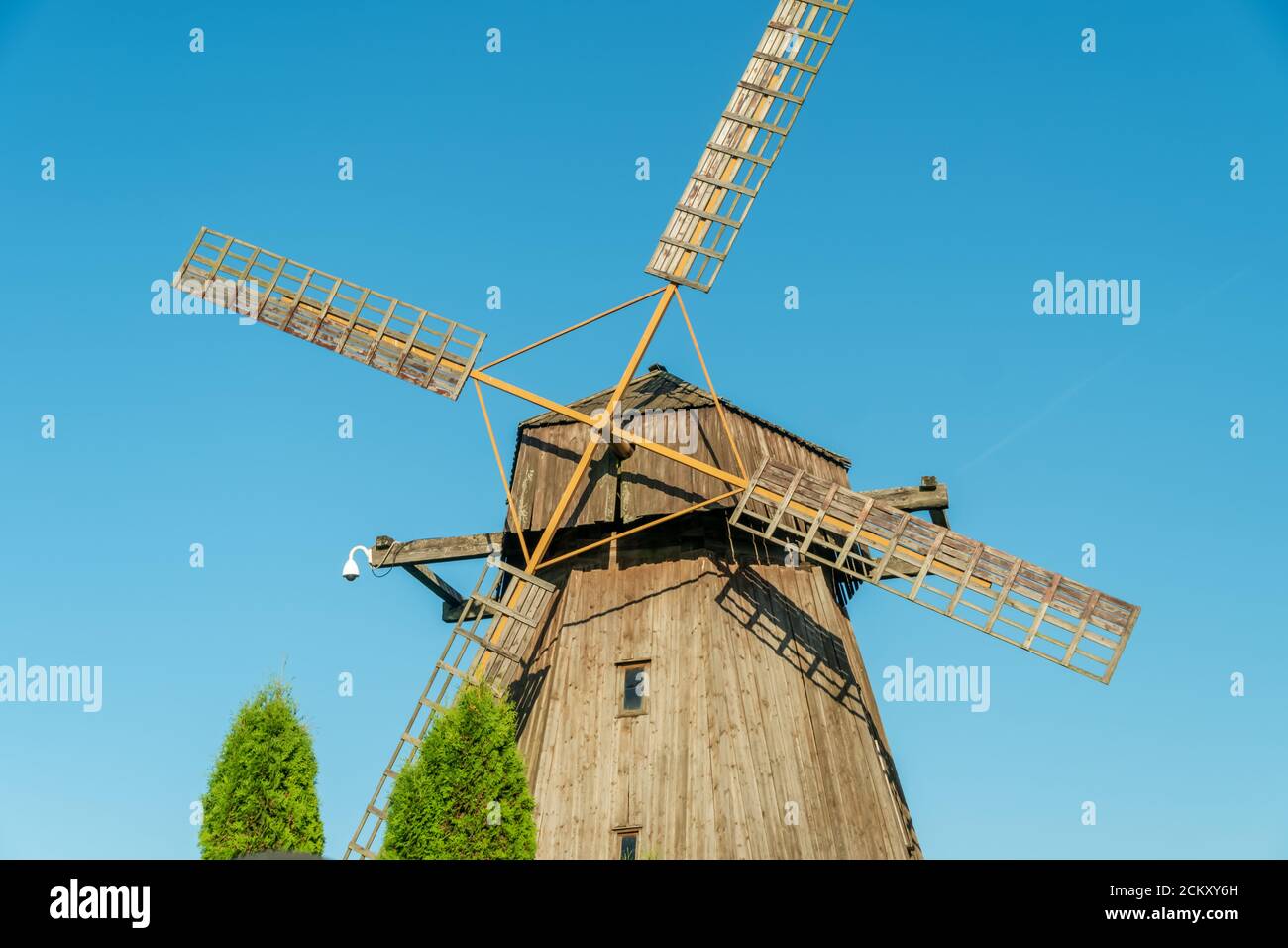 Windmill. Big wooden mill on blue sky background on Sunny summer day. Waste mill green arborvitae Stock Photo