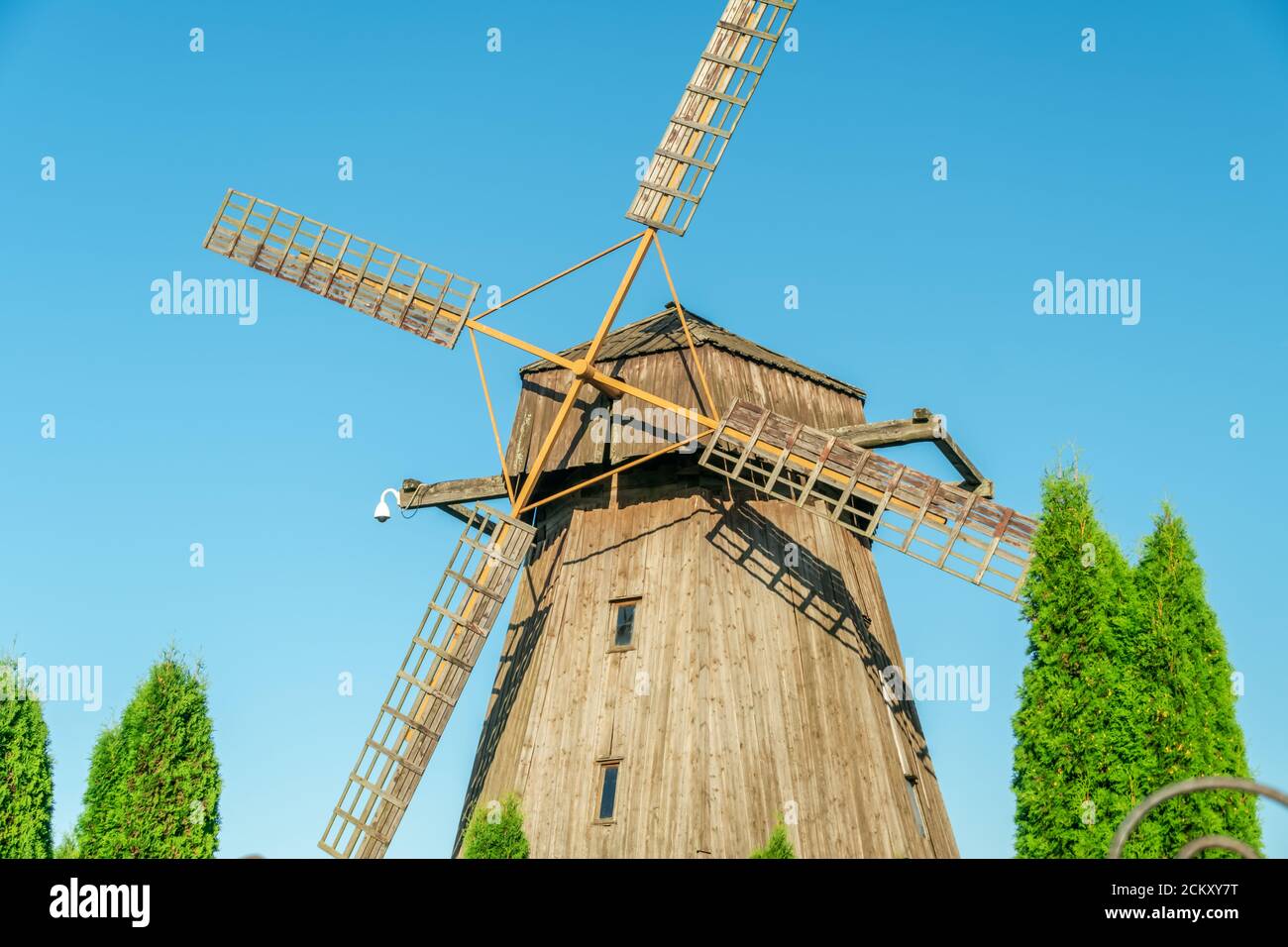 Windmill. Big wooden mill on blue sky background on Sunny summer day. Waste mill green arborvitae Stock Photo