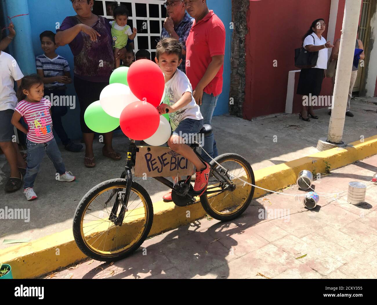 A child rides a bike adorned with balloons and a sign reading \