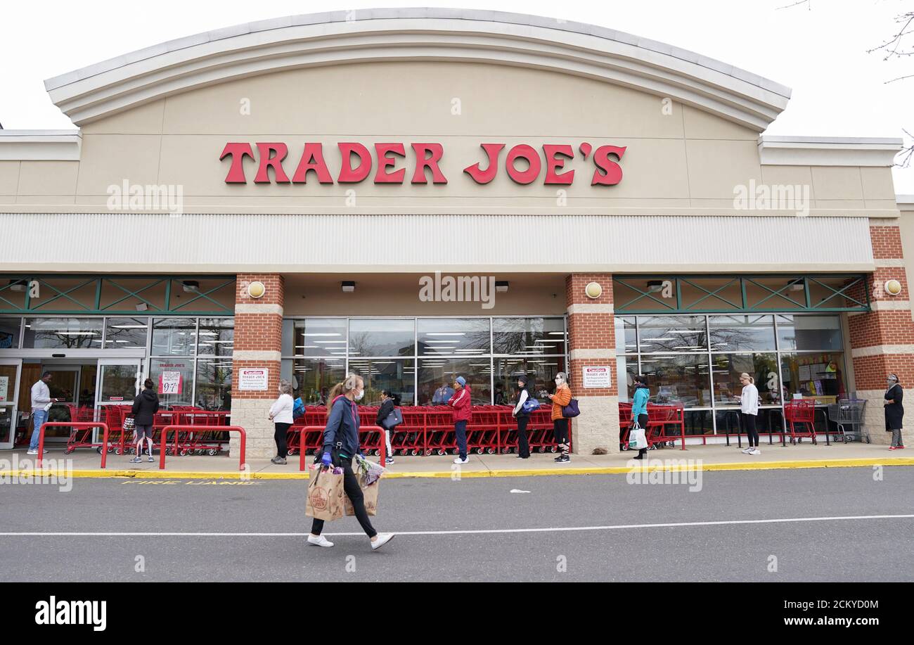 A shopper wearing a protective face mask passes near a self-distancing queue outside Trader Joe's, as they limited the amount of shoppers allowed in the store to help prevent the spread of coronavirus disease (COVID-19), in Bailey's Crossroads, Virginia, U.S., March 31, 2020.  REUTERS/Kevin Lamarque Stock Photo