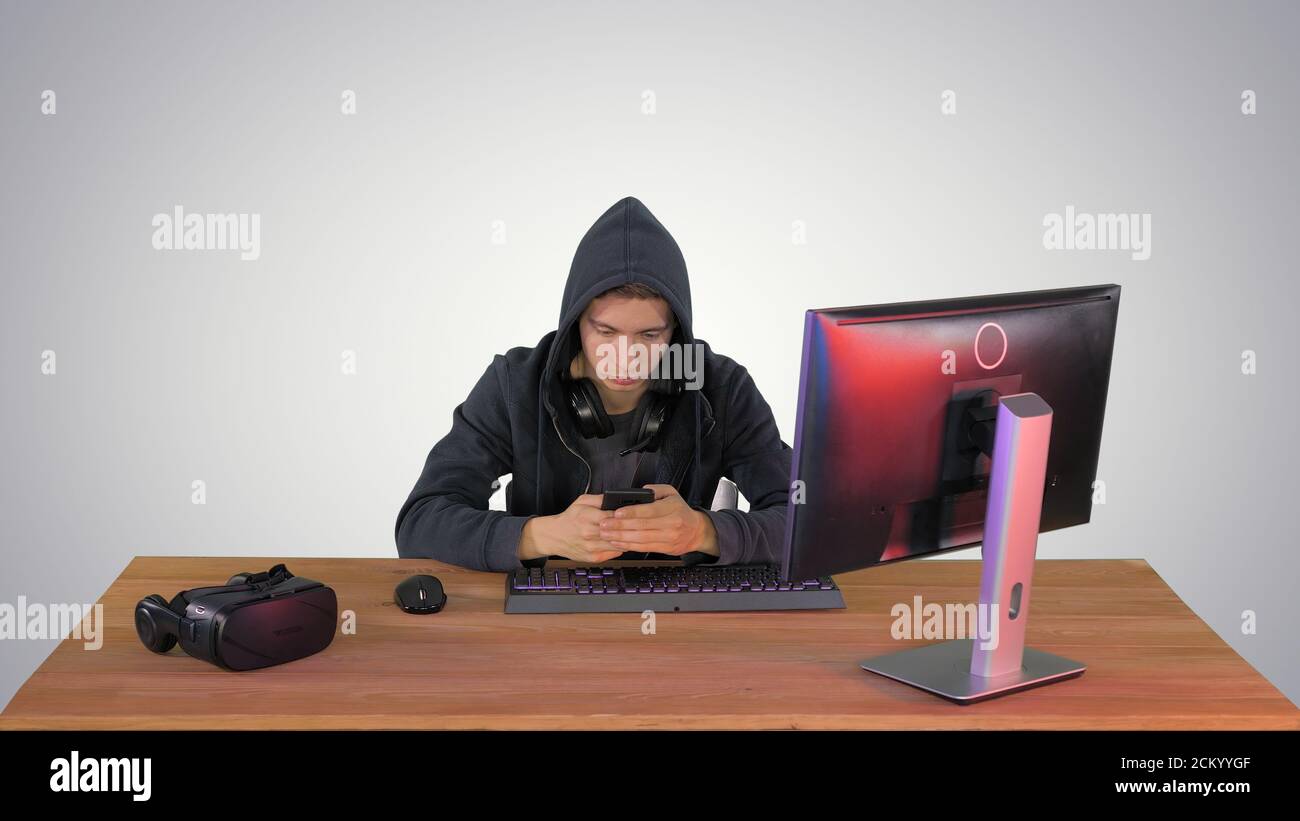 Hooded hacker using laptop and smartphone on gradient background Stock Photo