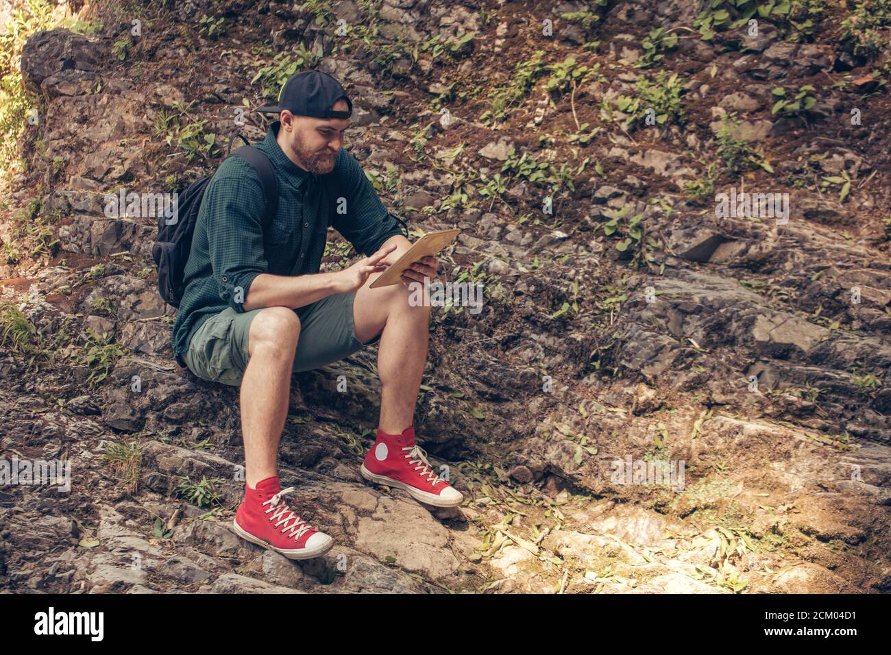 Bearded hipster man in trekking outfit, hiking through deep forest, resting  on ground during map download process using digital tablet Stock Photo -  Alamy