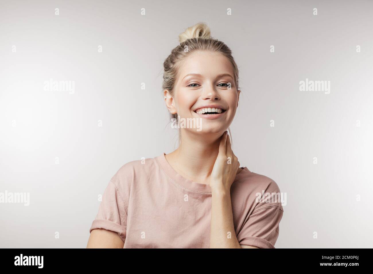 Positive attractive young woman casually dressed, with hair tired in knot, smiling at camera over white background with copyspace for advertisement. Stock Photo