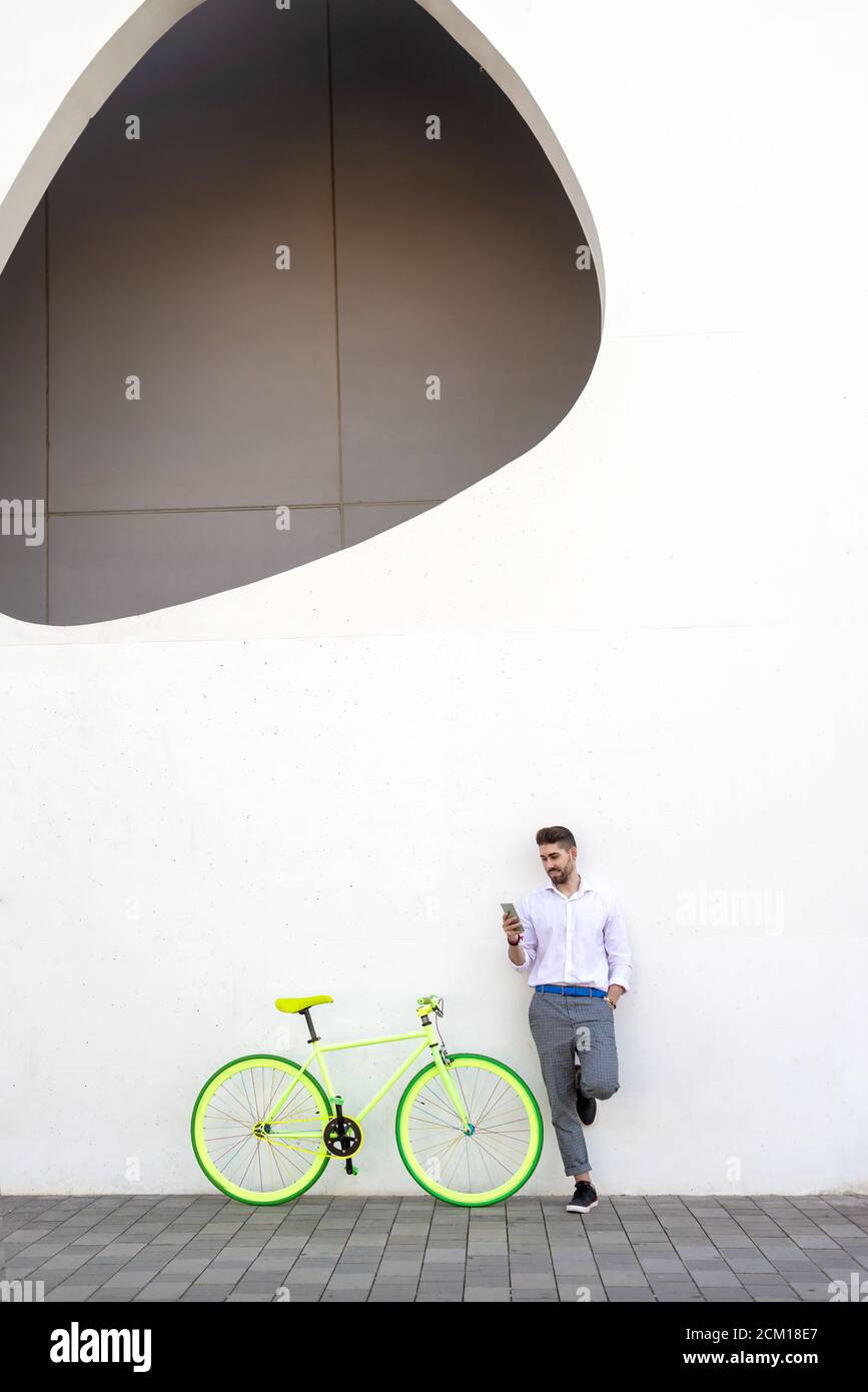 Young bearded man leaning against a white wall using the mobile phone Stock Photo