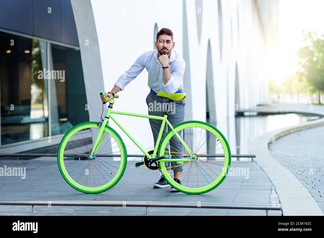 Young bearded man leaning on bicycle seat while looking at camera Stock Photo