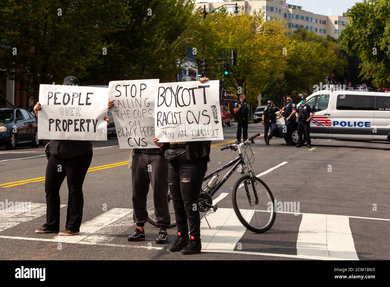 Washington, DC, USA, 16 September, 2020.  Pictured: Protesters hold signs that say CVS is racist and values people over proterty, while Metropolitan (DC) Police officers look on in the background.  The protest took place because the day before, the CVS store manager called police about two 'suspicious' black men.  Six Metropolitan (DC) Police officers detained the two men, ultimately releasing them after a search found no stolen items.  Given the substantial risk of violence when police are called on Black men, a number of people came to protest the manager's decision.  Credit: Allison C Baile Stock Photo