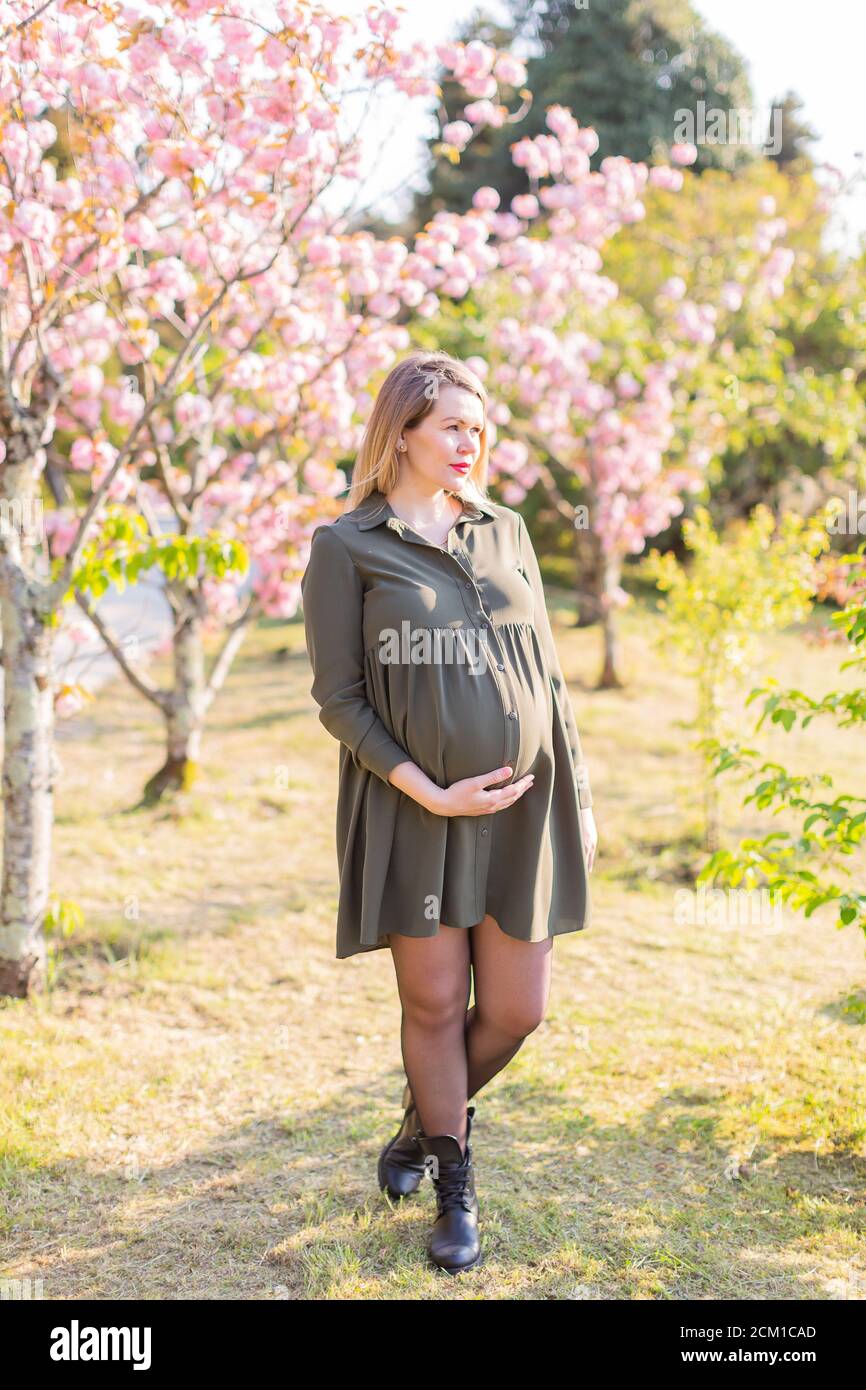 Gentle pregnant woman in the park at spring with cherry blossom trees ...
