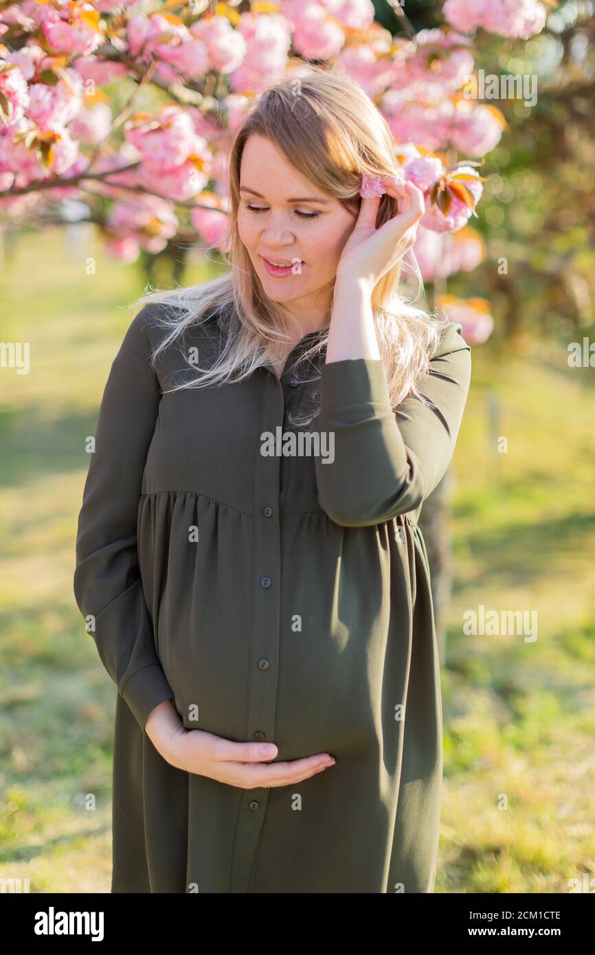 Gentle pregnant woman in the park at spring with cherry blossom trees ...