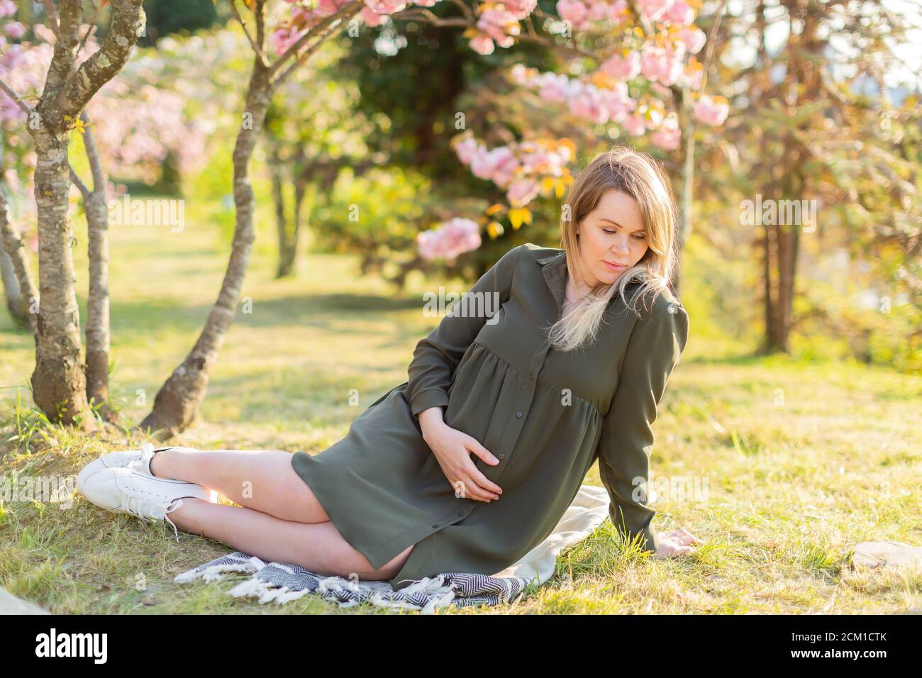 Gentle pregnant woman in the park at spring with cherry blossom trees ...