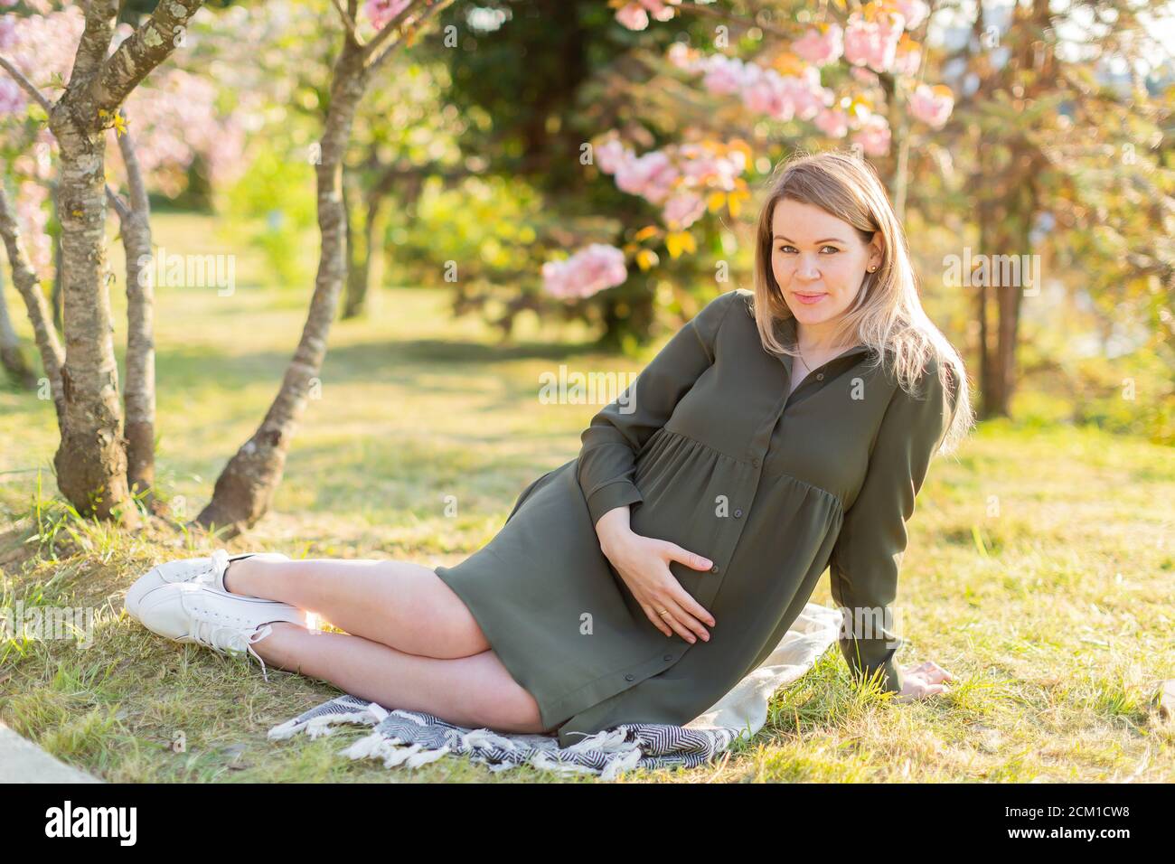 Gentle pregnant woman in the park at spring with cherry blossom trees ...