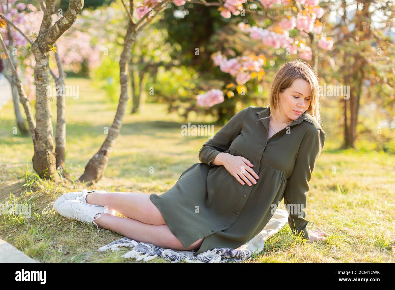 Gentle pregnant woman in the park at spring with cherry blossom trees ...