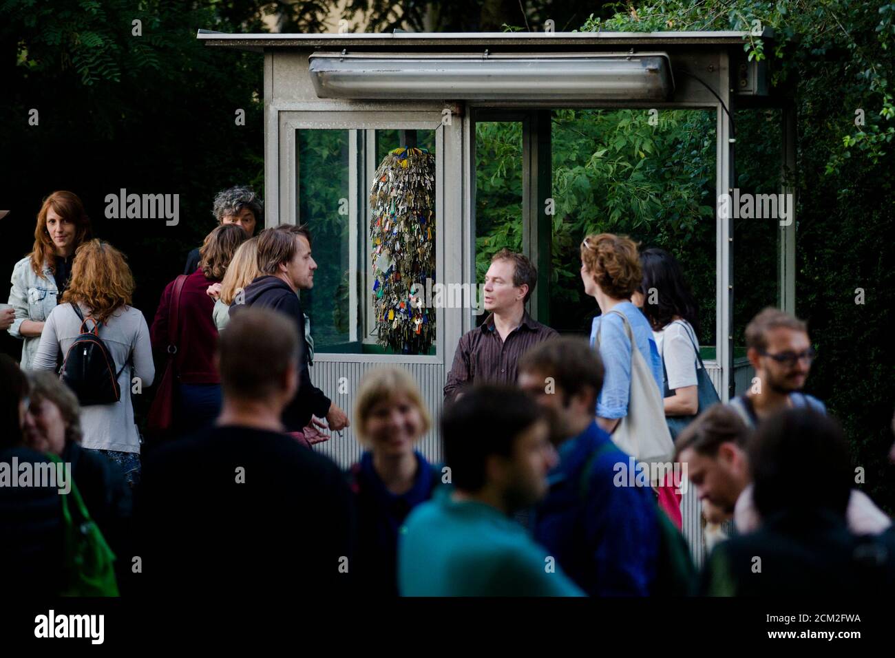 People attend the opening of an installation of keys, used in Stasi police barracks, by Sonya Schoenberger (L), that is installed inside Christoph Zwiener's exhibition project 'ADN Guard House' in Berlin July 11, 2014. A German artist has turned a tiny surveillance booth used by the communist regime in the former East Germany to monitor citizens into an art exhibit and venue, which will be installed in a museum near Los Angeles dedicated to the Cold War. The one-person guardhouse measuring 2 m by 1 m (2 yards by 1 yard) was originally located in the parking lot of state-run news agency ADN so  Stock Photo