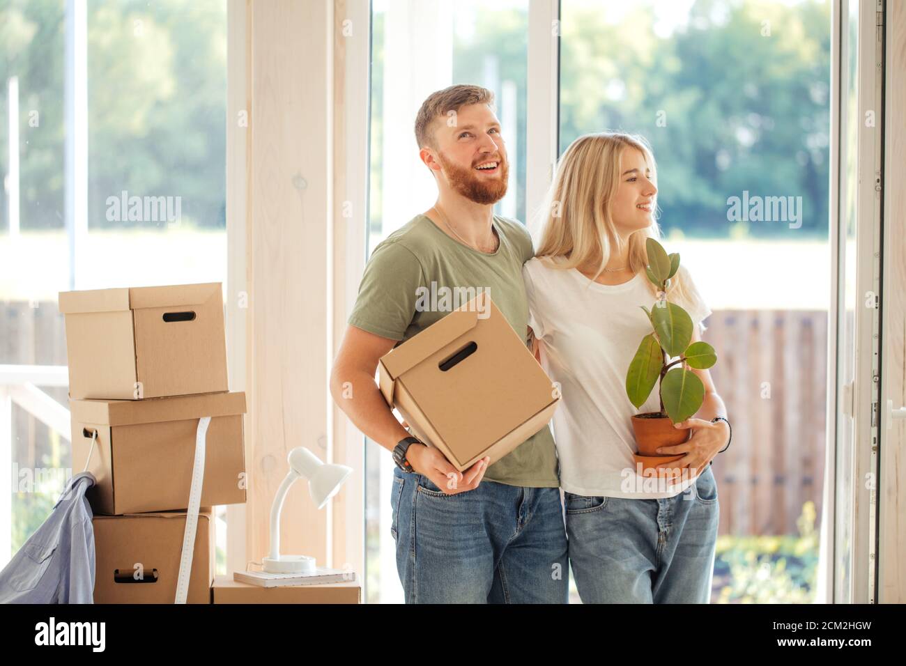 Happy smiling couple moving in new house and carrying carton boxes ...