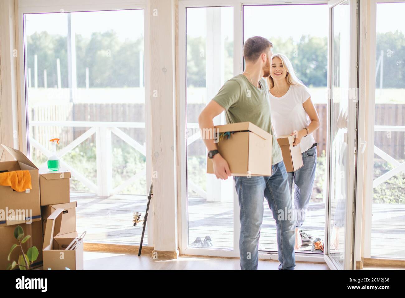 Happy smiling couple moving in new house and carrying carton boxes ...