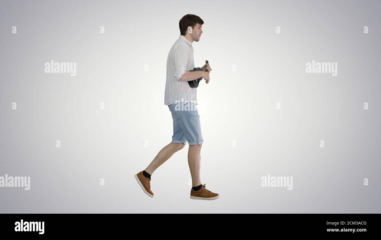 Young man playing ukulele while walking on gradient background. Stock Photo