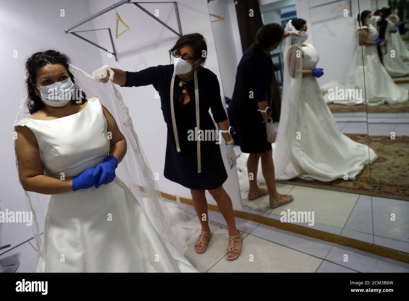 Olga Prades helps bride Isabel Jimenez try on a wedding dress, as they both  wear protection masks and gloves, at her bridal shop Innovias, on the first  day that some small businesses