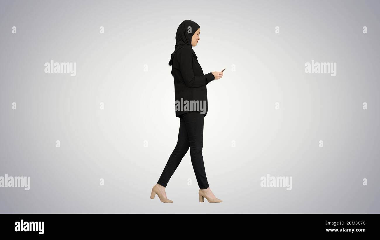 Pretty woman in hijab walking and counting money on gradient bac Stock Photo