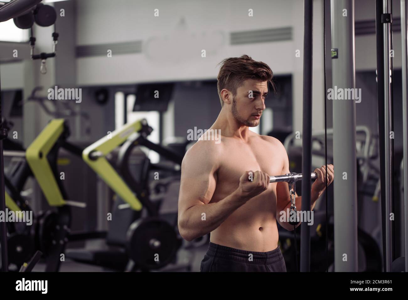 Caucasian handsome athletic male bodybuilder performing exercise with gym-apparatus, working out on broadest muscle of back Stock Photo