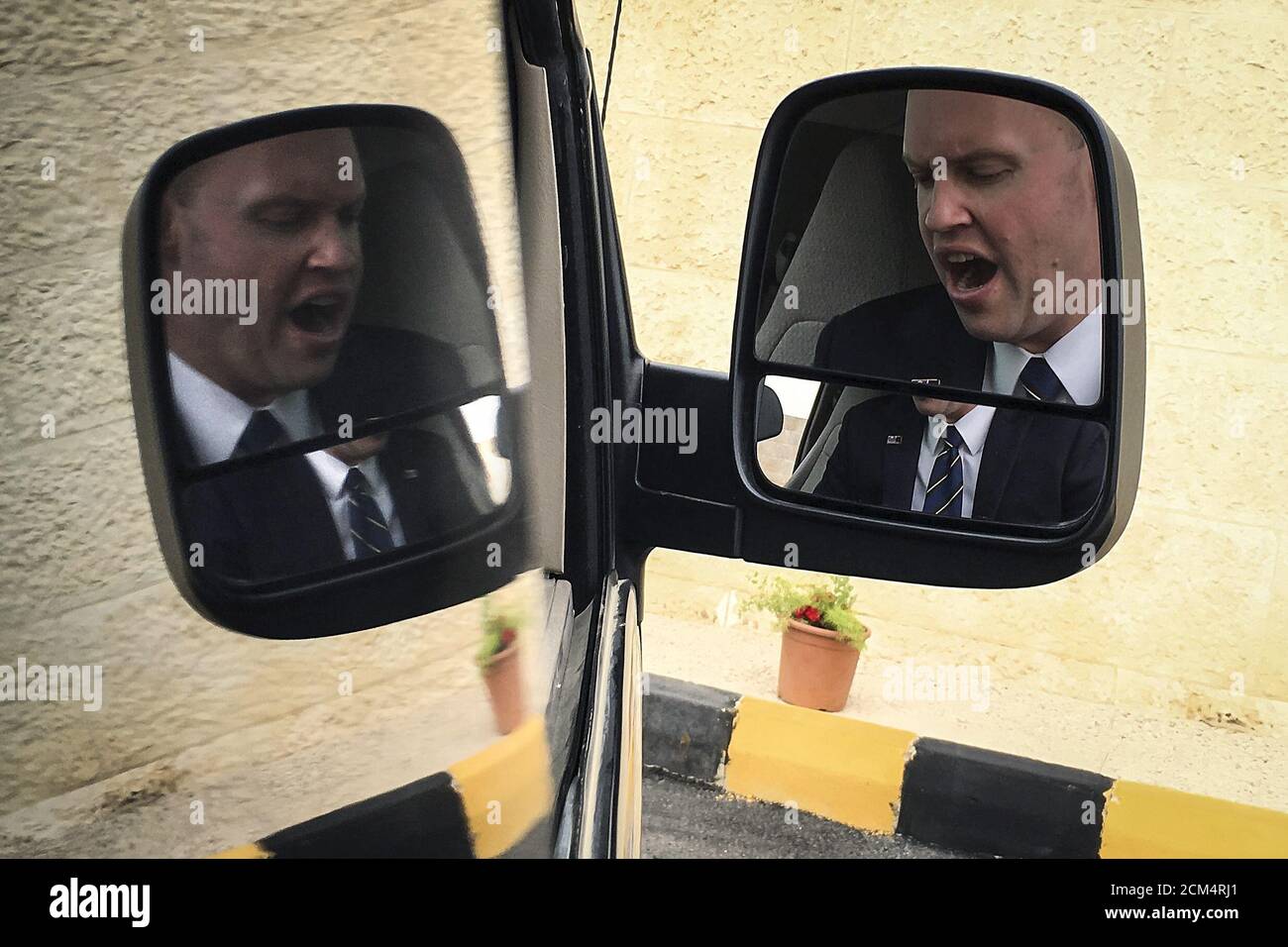 A U.S. official is reflected on the side mirror of a press pool van while he yawns as the van was held for a time at the main entrance to King Abdullah II's palace in Amman, October 24, 2015. REUTERS/Carlo Allegri Stock Photo