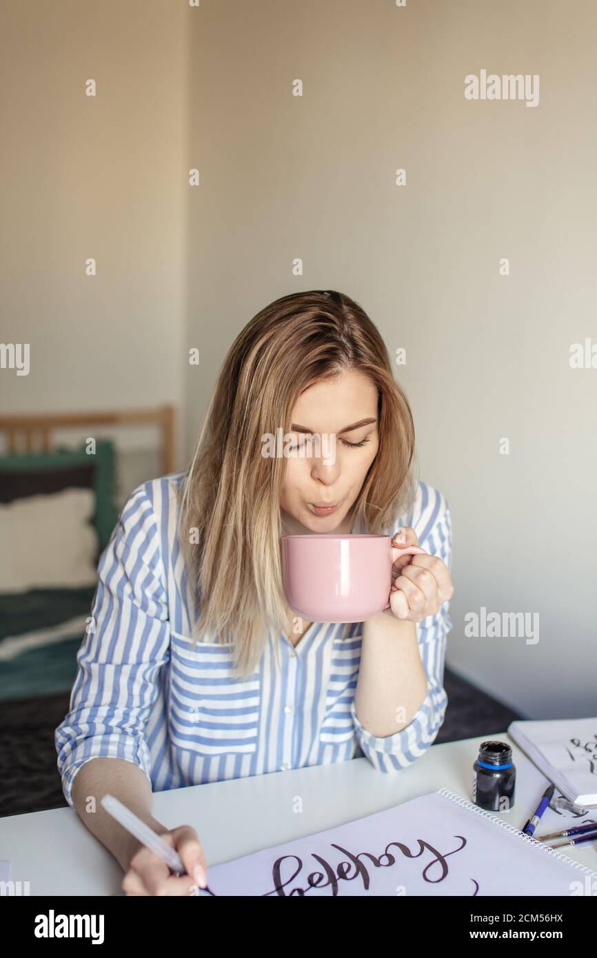 Close up photo of woman writing beautiful notes on paper on white desk while drink coffee or tea Stock Photo