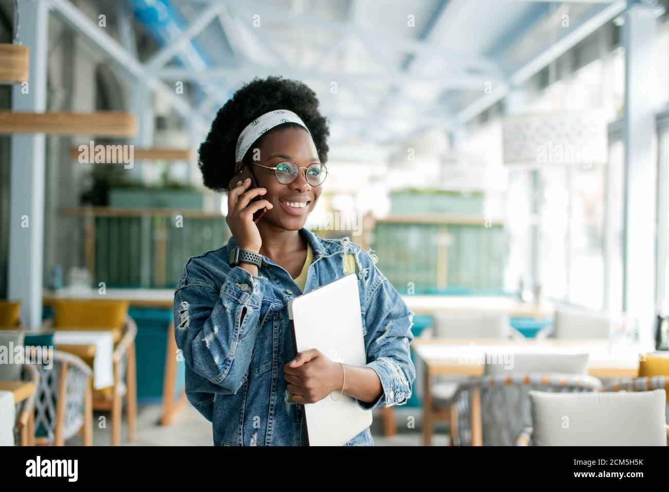 Cute dark skinned female entrepreneur holding digital tablet, making call while visiting coffee shop, inviting a candidate to a job interview. Stock Photo